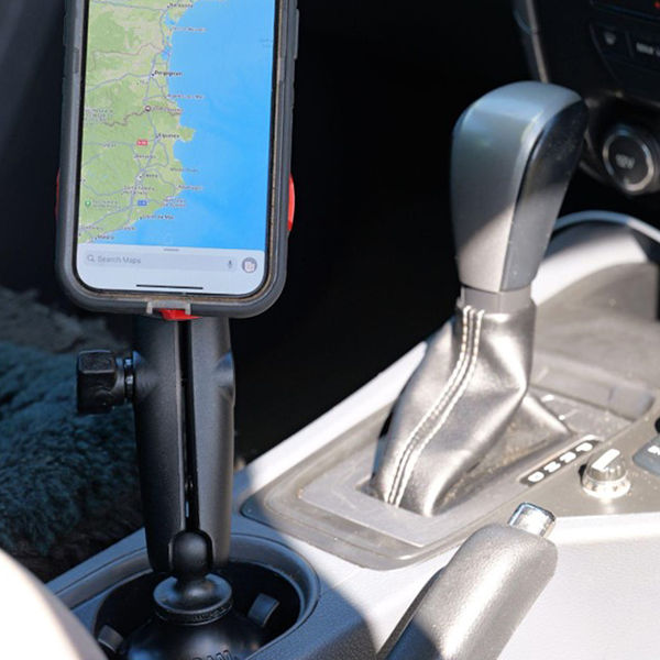 Inside a car showing a RAM A-CAN cup holder mount with a medium arm holding a phone.